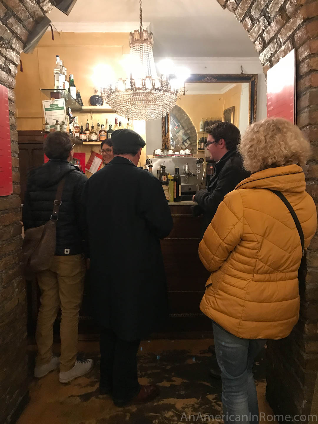 two men and a woman in a yellow coat standing in a small bar