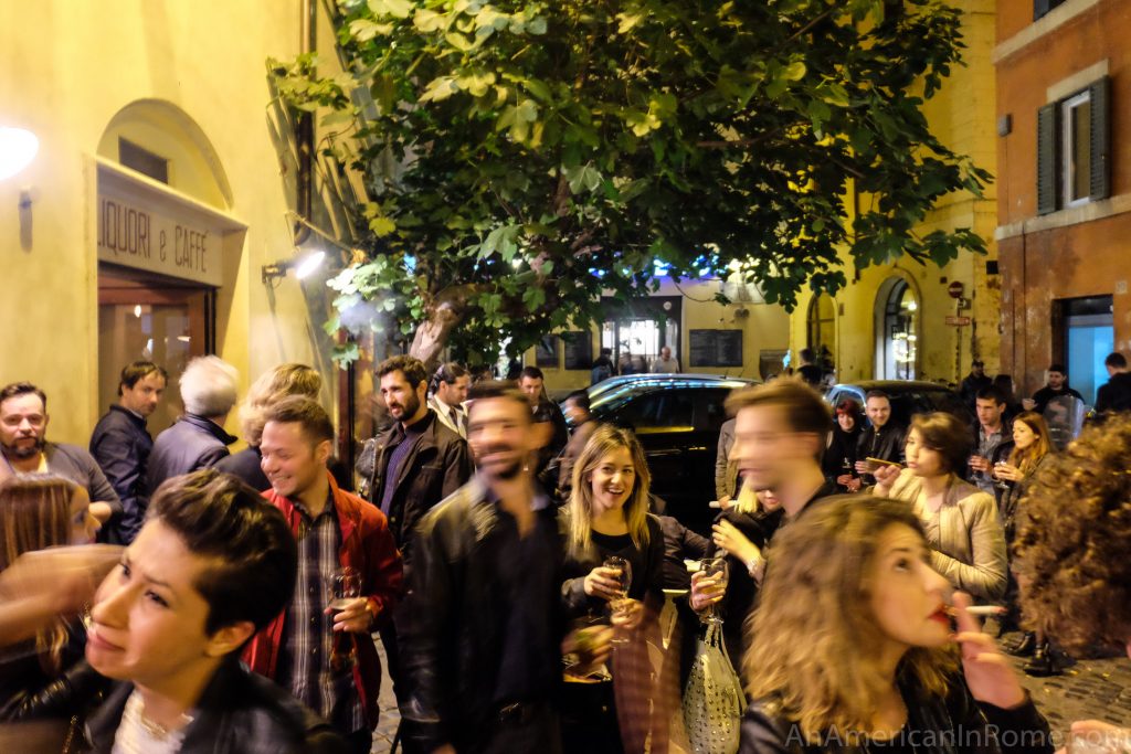 revelers moving in and out of focus with drinks in their hands outside of bar del fico