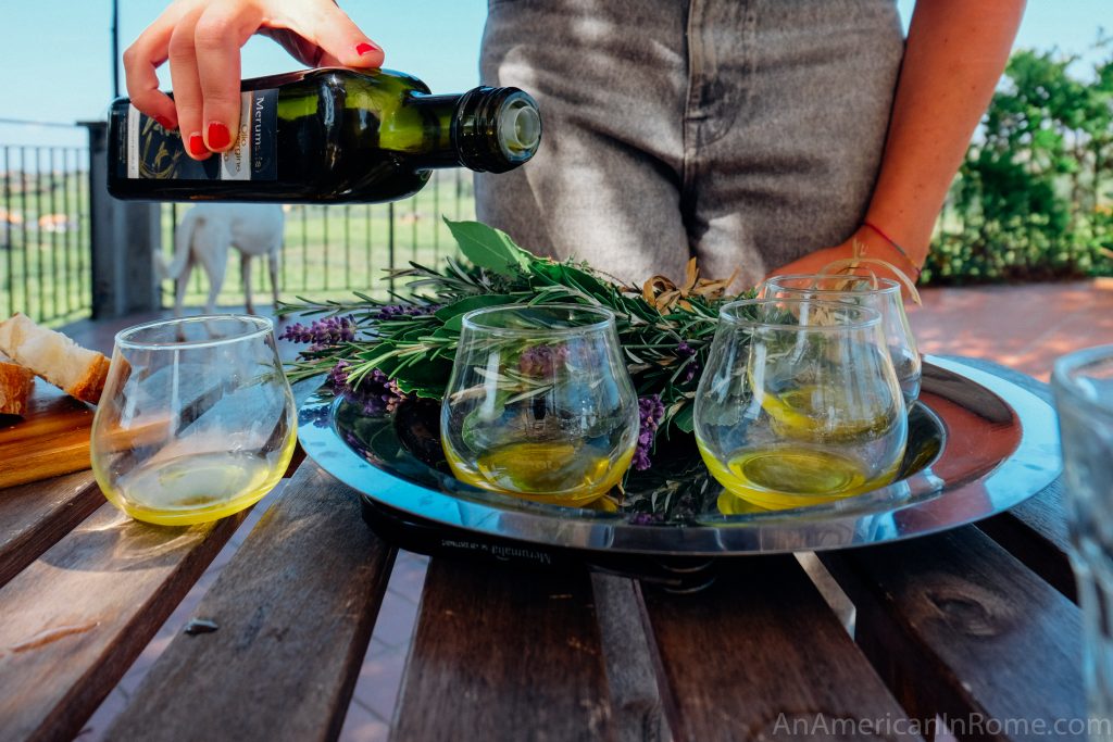 a hand pouring extra virgin olive oil into two tasting glasses on a silver platter