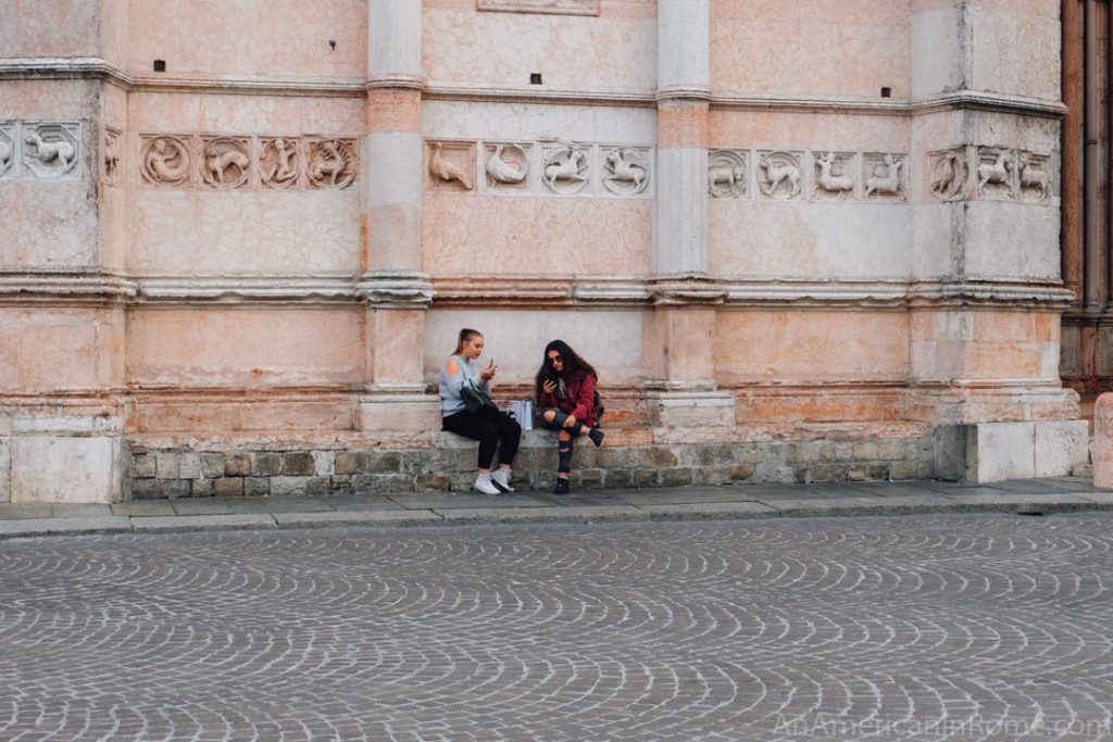 two girls sit on a bench along the exterior of the baptistry in Parma italy