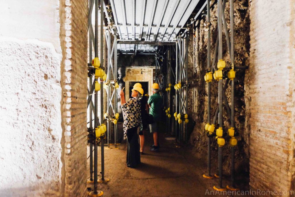 a woman in a hard hat takes a photo under scaffolding in the Domus Aurea