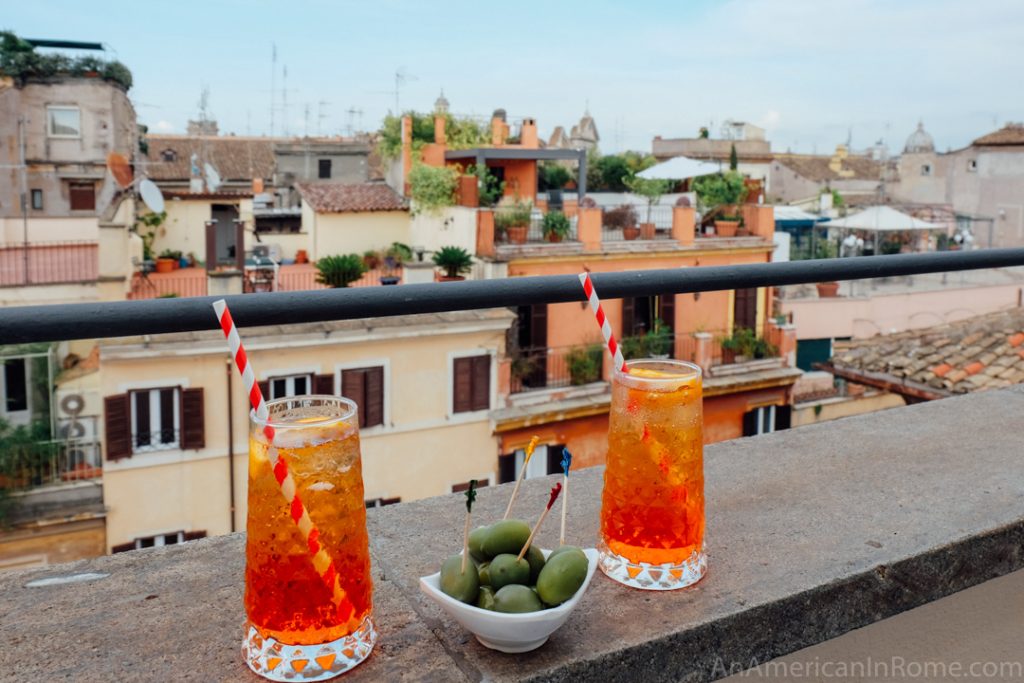 two red spritz cocktails on the edge of a rooftop in Rome with a bowl of green olives