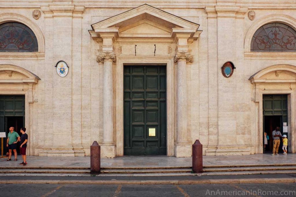 white stone exterior of the church of San Luigi dei Francesci with one closed main door and a smaller open door on either side