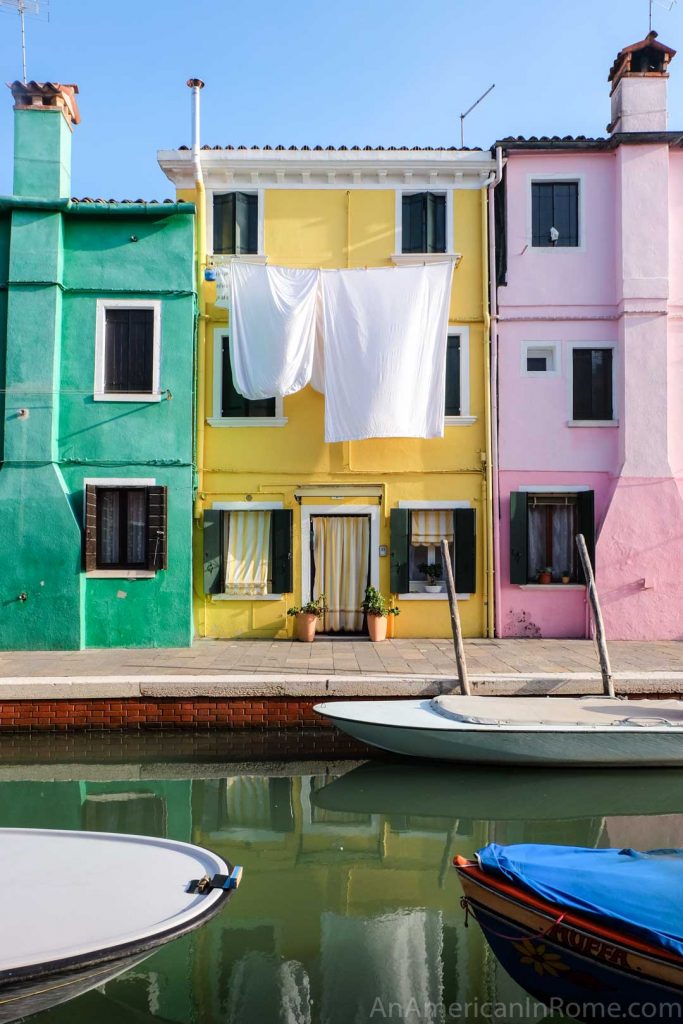 Green yellow and pink homes with white laundry outside on the island of Burano near Venice