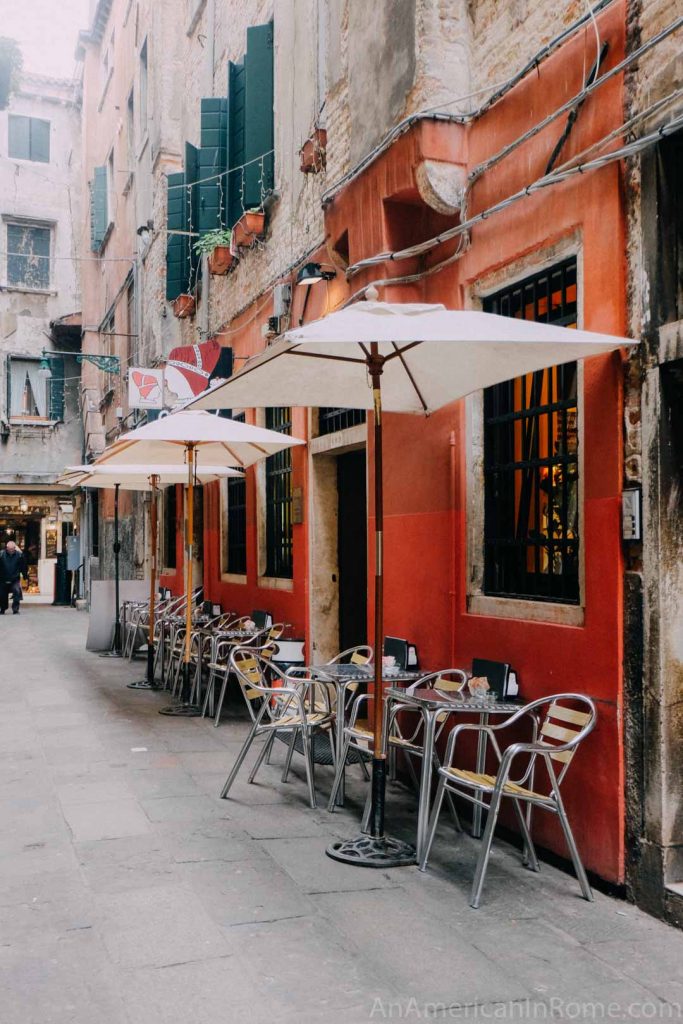 Outside of caffe del doge in Venice with orange walls and white umbrellas over outdoor tables