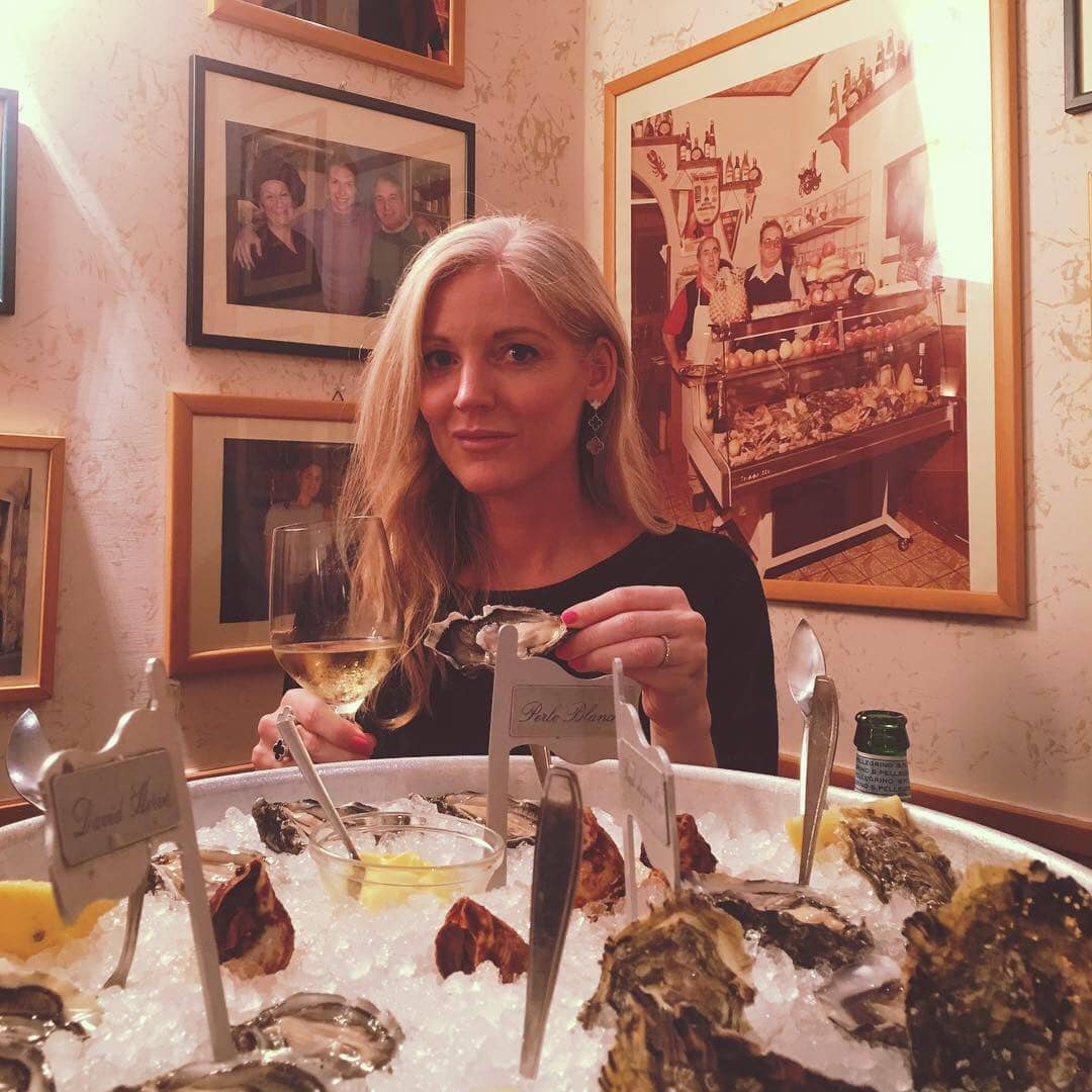 Joanne holding an oyster and a glass of wine at Da Benito e Gilberto with photographs on the wall behind