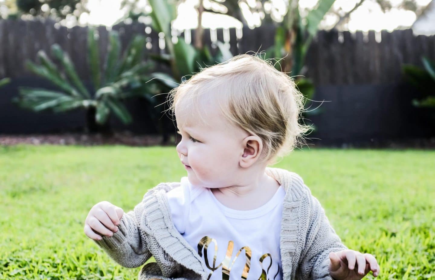 blonde haired baby on the grass in a shirt that says ONE in gold script