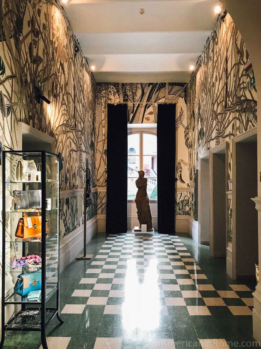 patterned wallpaper and a statue at the end of hallway lit by a window in Roma Luxus house