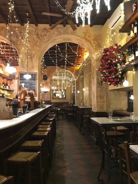 Rome restaurant with long dining room strung with lights and with dark wood stools at the bar