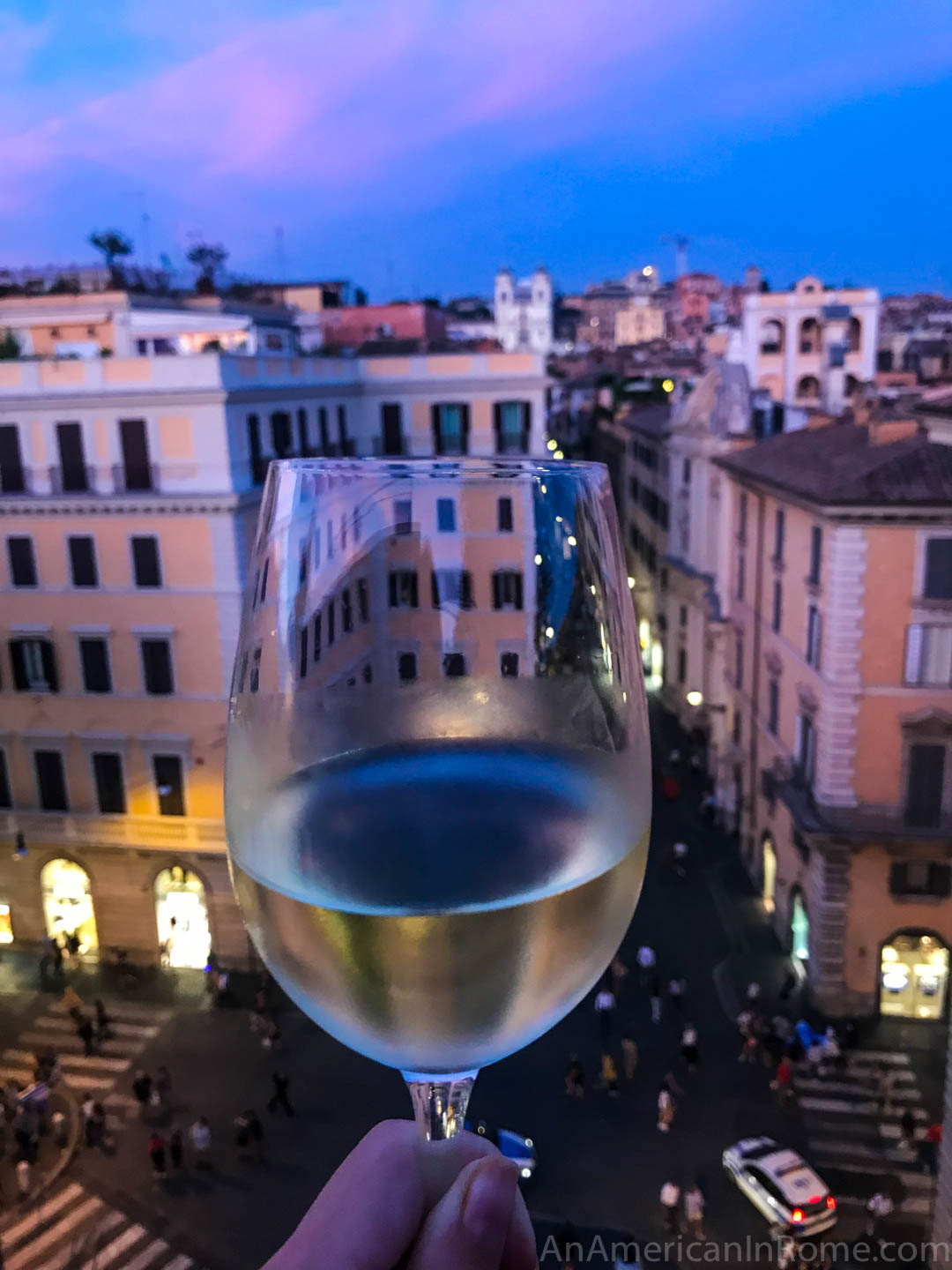 glass of white wine held up to Rome skyline