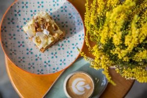 cake on a plate with a foamy cappuccino and yellow flowers