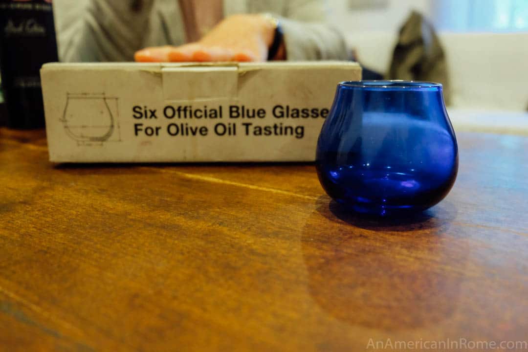 mėlynos alyvuogių aliejaus skonio taurė priešais dėžutę, kurioje aprašyta, kas tai yra